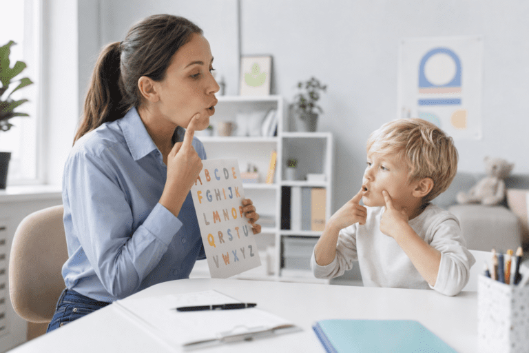 A woman and a young boy practice speech sounds together; the woman holds a chart with the alphabet while both point to their mouths - Can Screen Time Cause Speech Delay in Toddlers?